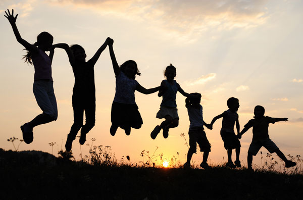 a group of children holding hands and jumping in front of a sunset.