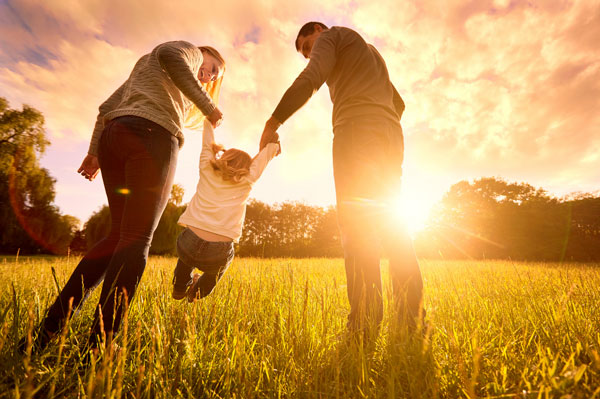 Parents holding their young child in a field with a sunset.